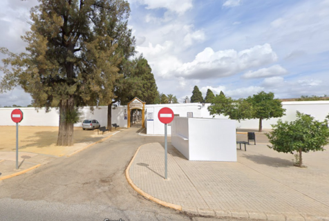 Cementerio Municipal San Francisco de El Viso del Alcor, Sevilla. www.cementerio.info En la imagen vemos la entrada al Cementerio Municipal San Francisco de El Viso del Alcor, en Sevilla. Un camino serpenteante con bordillos conduce a una puerta de acceso, que está enmarcada por un arco ornamentado y una pequeña estructura con tejado a dos aguas. La entrada al cementerio está flanqueada por muros blancos, con dos señales de tráfico de "prohibido el paso" a ambos lados, indicando que es una vía de sentido único o restringido. Hay árboles grandes y frondosos a la izquierda, lo que sugiere que el cementerio tiene áreas verdes maduras. En la parte derecha, se observa una zona más abierta con árboles más pequeños y vegetación baja. El cielo está parcialmente nublado, lo que aporta una atmósfera tranquila y reflexiva. La combinación de vegetación, el diseño arquitectónico de la entrada y la presencia de los muros blancos ofrecen una imagen que es típica de los cementerios tradicionales de la región.